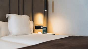 A neatly made bed with white linens and a dark headboard. A bedside table with a black lamp and a green sign reading "Wellness Room" is visible.