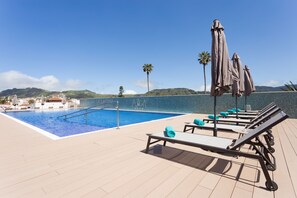 A rooftop pool area with lounge chairs and umbrellas, a clear blue sky, and a view of distant hills. - La Laguna Gran Hotel (San Cristóbal de La Laguna)