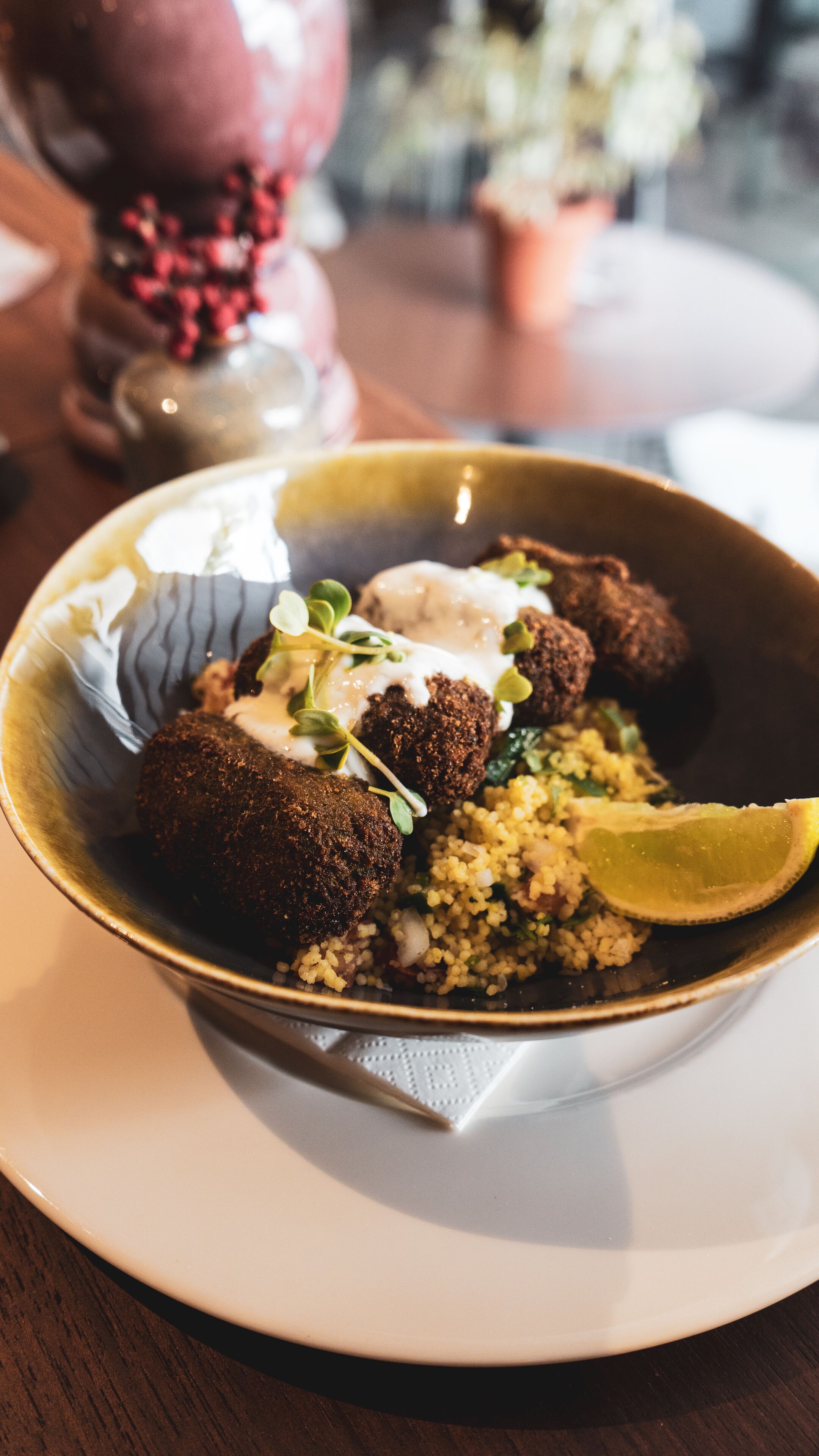 A bowl of food with falafel balls, a slice of lime, and a creamy sauce, served on a plate with a napkin underneath.