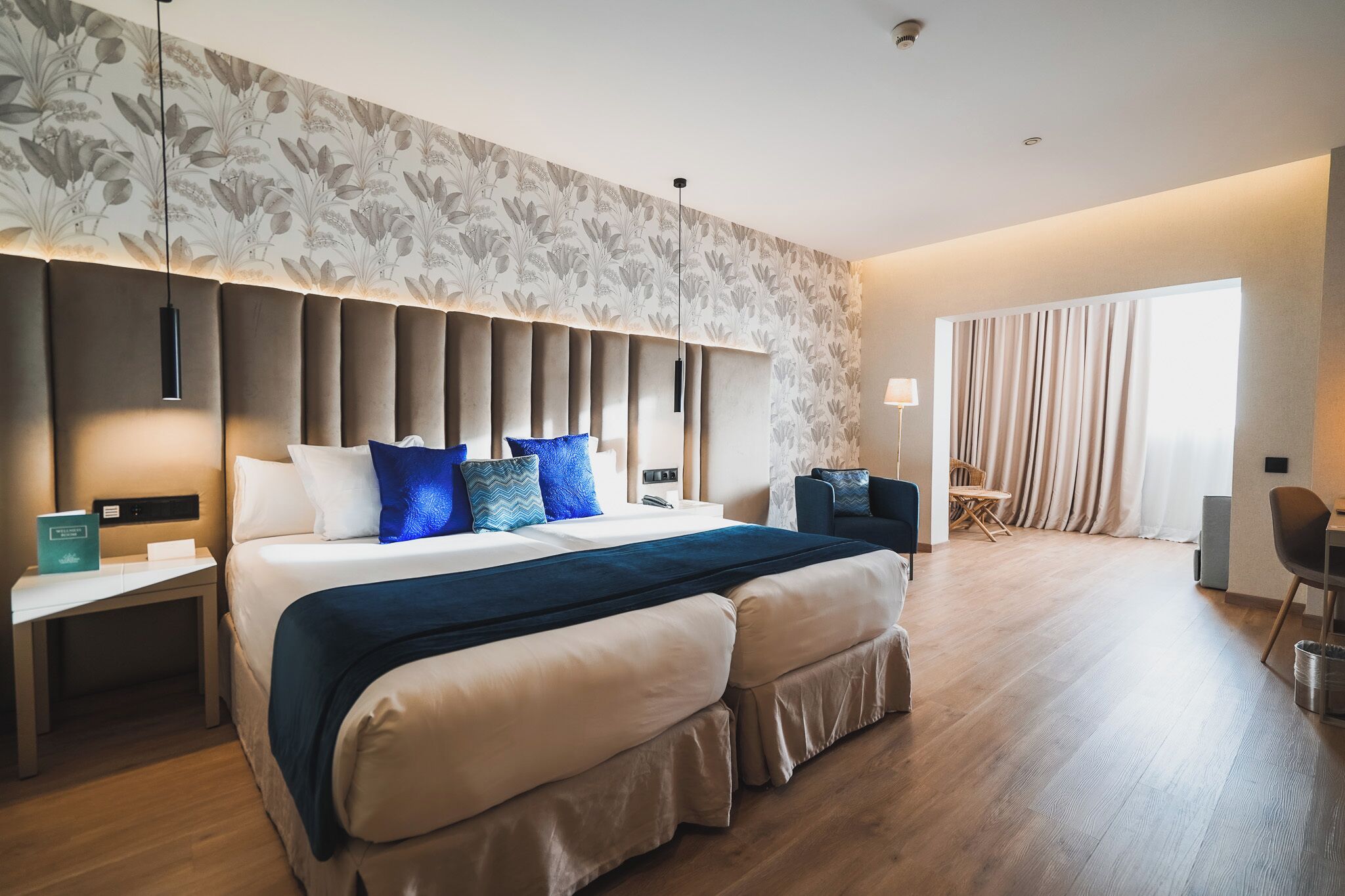 A modern hotel room with a large bed, a nightstand, a desk, and a seating area with a chair and a table.