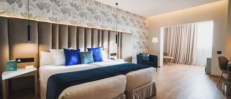 A modern hotel room with a large bed, a nightstand, a desk, and a seating area with a chair and a table.