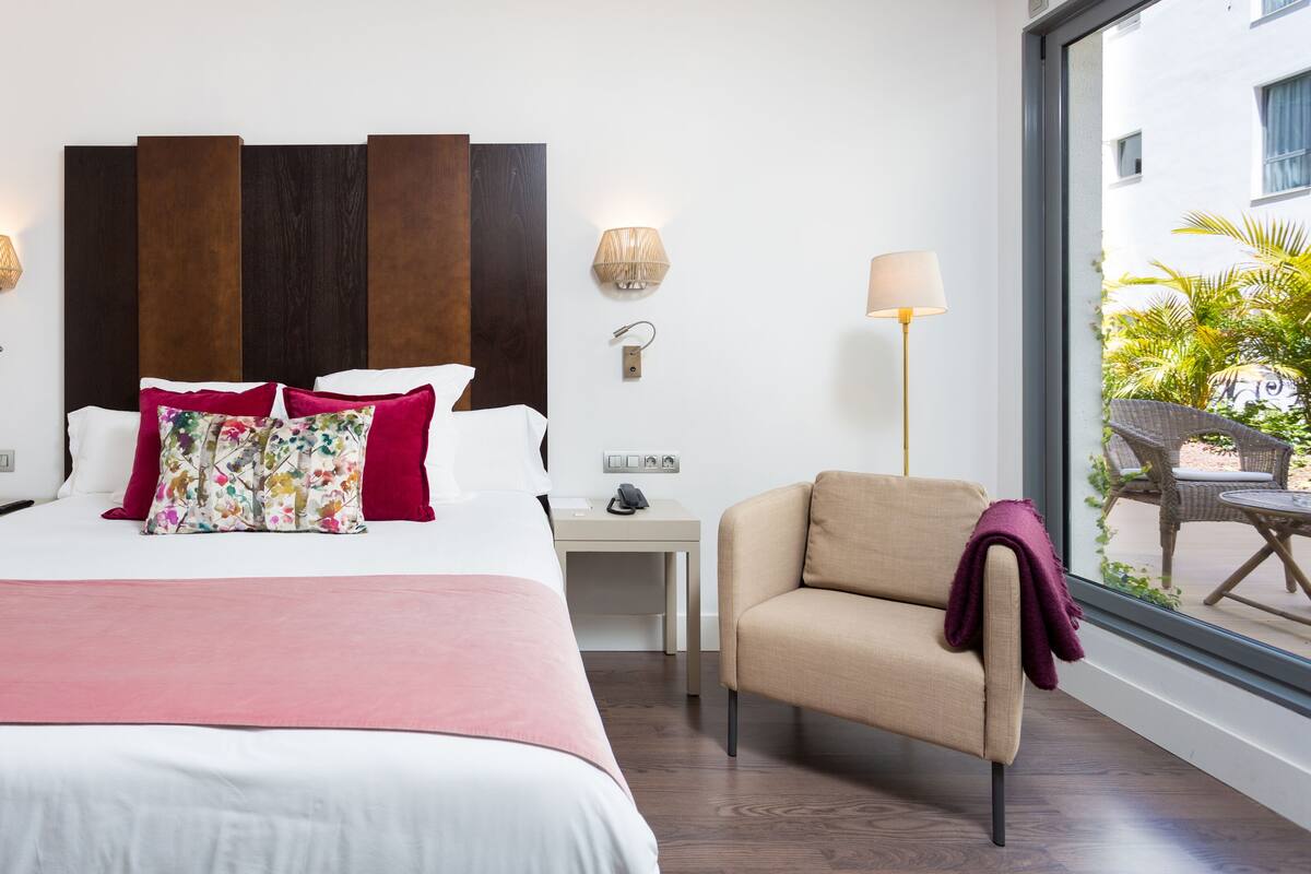 A hotel room with a large bed, a chair, a nightstand, and a lamp.