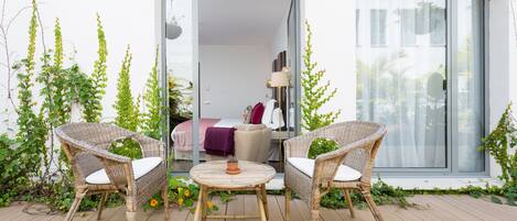 Un balcone con mobili in vimini, una pianta in vaso e vista su una stanza con un letto e una lampada.