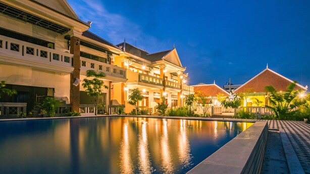 A large, well-lit swimming pool with a traditional architectural building in the background. - Amour d'Angkor (Siem Reap)