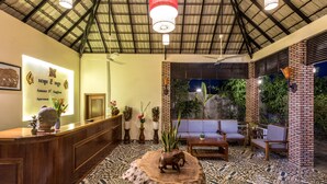 A reception area with a wooden reception desk, a large elephant sculpture on a tree stump, a sofa, and a brick pillar. - Amour d'Angkor (Siem Reap)