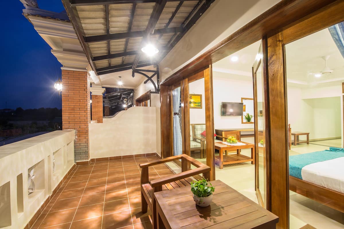 A spacious balcony with a wooden table and chairs, a potted plant, and a view of the interior.