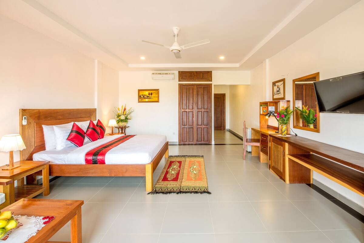 A hotel room with a bed, bedside table, lamp, TV, desk, and a large mirror.