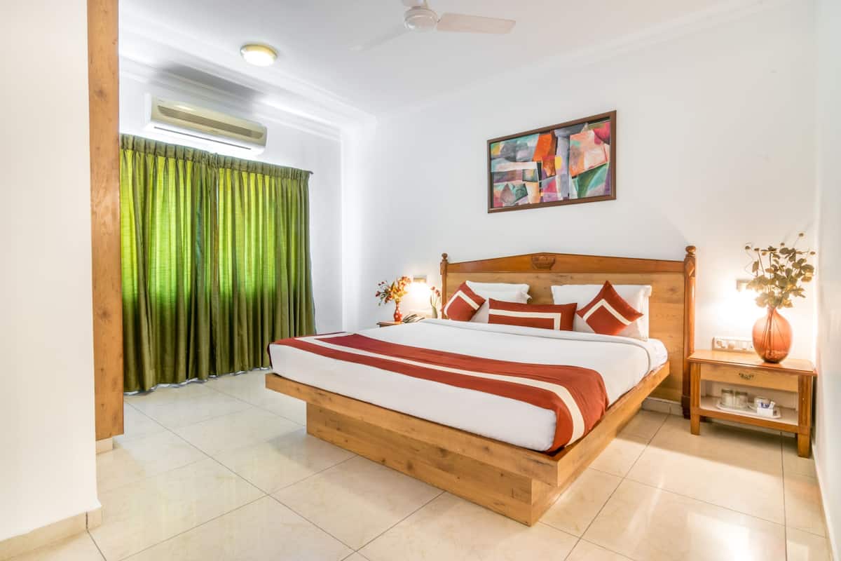 Quarto com cama de madeira, cortinas verdes, ventilador de teto, um quadro e mesa de cabeceira com um vaso.