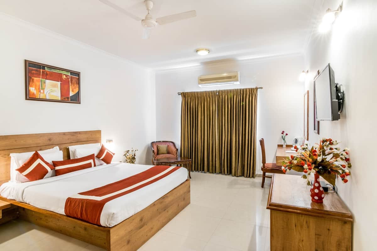 Quarto de hotel com uma cama, uma cadeira, uma escrivaninha, um vaso com flores e um quadro na parede.