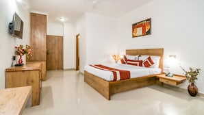 A bedroom with a wooden bed, bedside tables, a desk, a TV mounted on the wall, and a ceiling fan. - Octave Hotel Double Rd (Bengaluru)