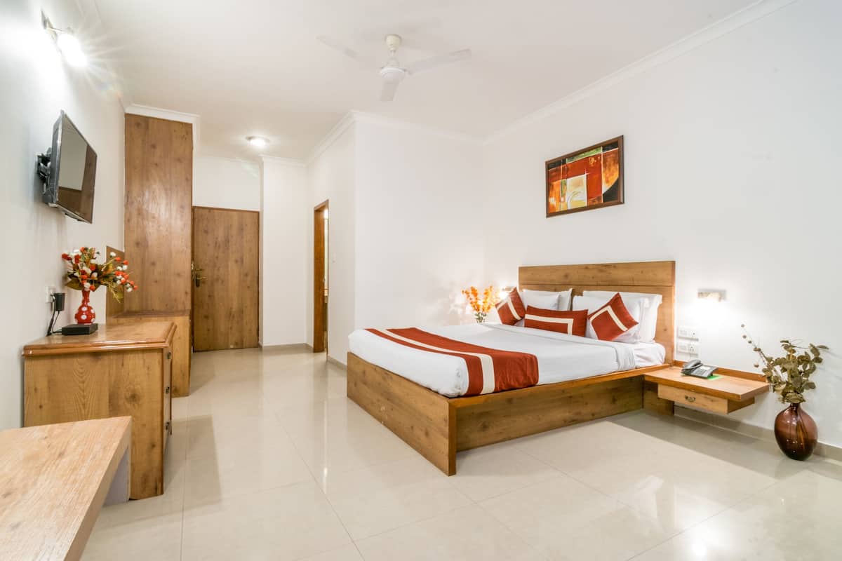 Quarto com cama de madeira, mesas de cabeceira, escrivaninha, TV fixada na parede e ventilador de teto.