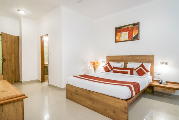 Un dormitorio con cama de madera, paredes blancas, un cuadro y una mesita de noche con lámpara.