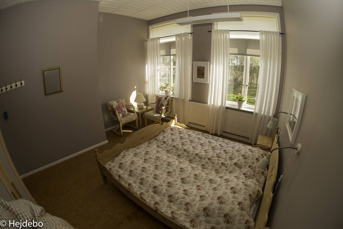 A bedroom with a bed, a chair, a table with a lamp, and a window with curtains.