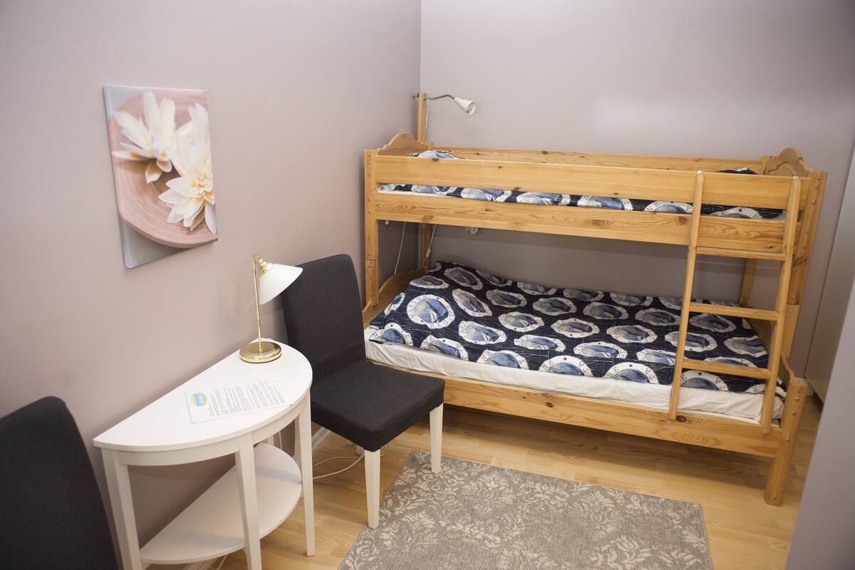 A bunk bed with a patterned mattress, a desk with a chair, a lamp, and a floral artwork on the wall.