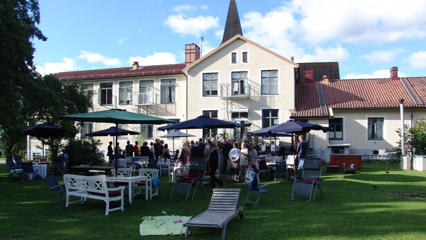 Un événement en plein air avec des tables et des chaises, des parasols et une pelouse devant un bâtiment doté d’une tour.