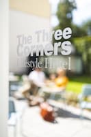 A blurred view of an outdoor seating area with tables and chairs, and the text "The Three Corners Lifestyle Hotel" is visible.