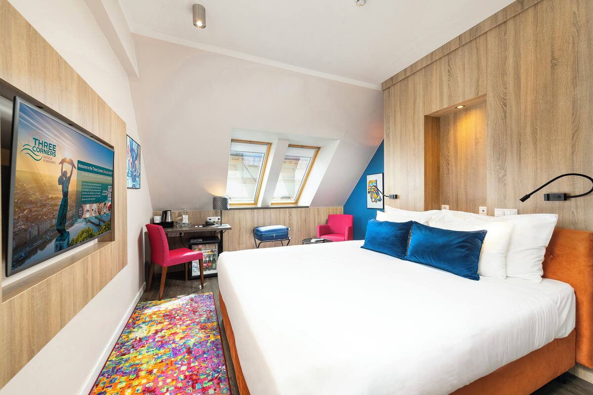 Moderni hotellihuone, jossa on suuri sänky, työpöytä, tuoli ja värikäs matto.
