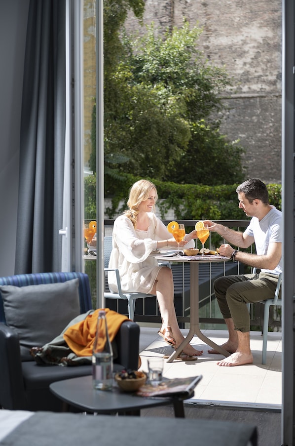 A couple dining at an outdoor table with a view of greenery and a brick wall. - Three Corners Lifestyle Hotel (Budapest)