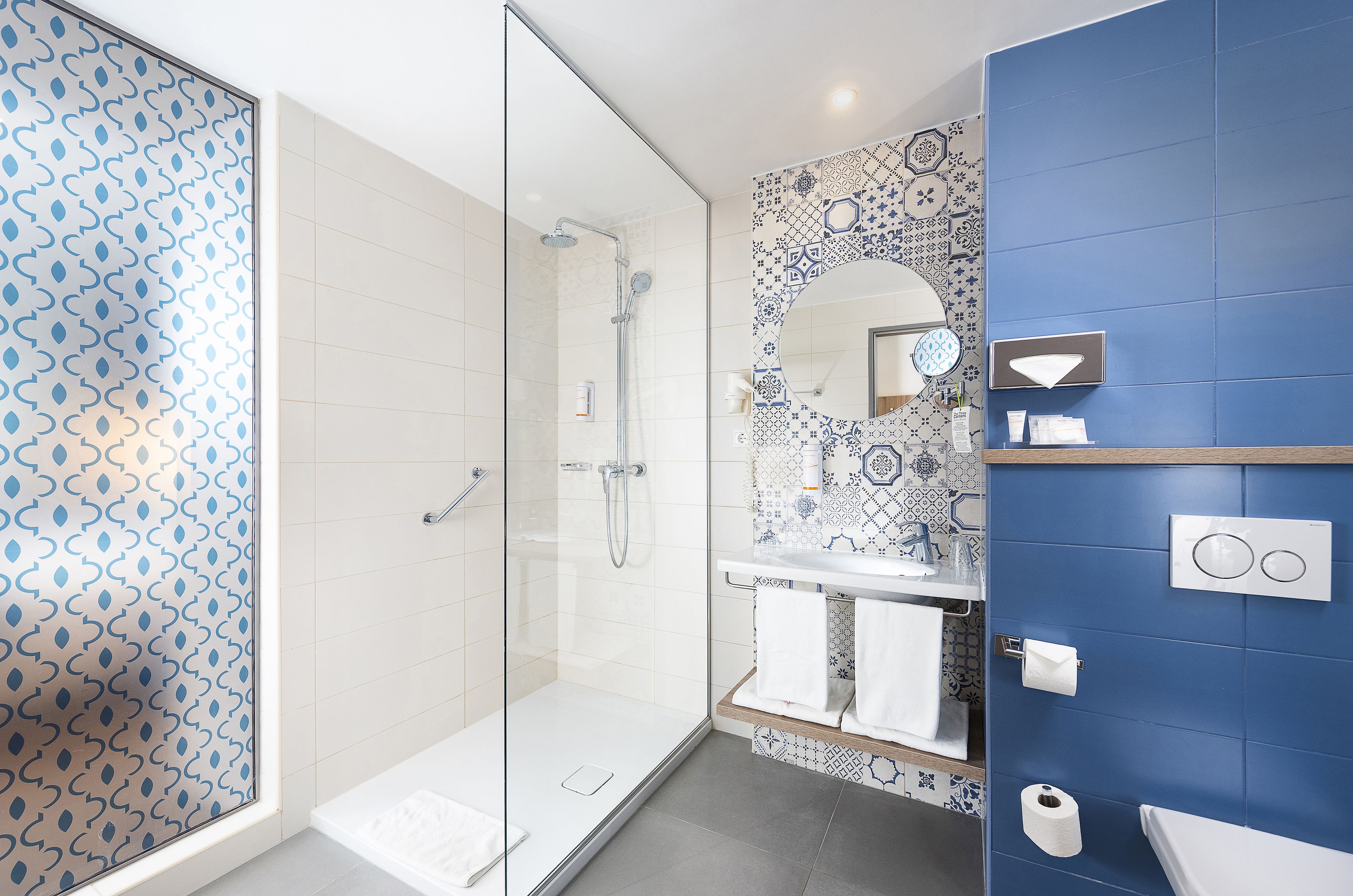 Un baño moderno con cabina de ducha de vidrio, un salpicadero de azulejos estampados y una pared de acento azul.