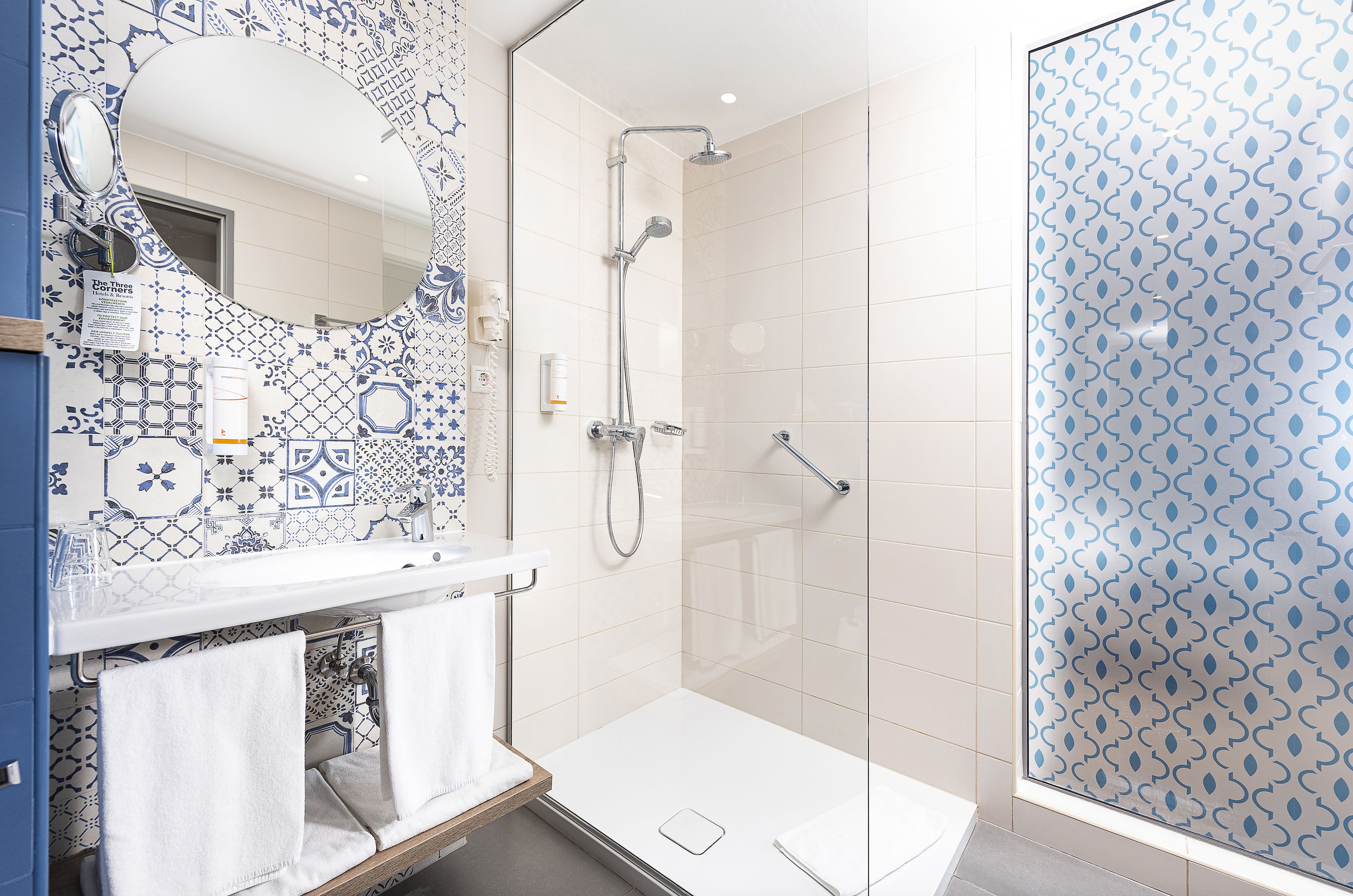 A bathroom with a shower, a sink with a mirror, and patterned tiles.