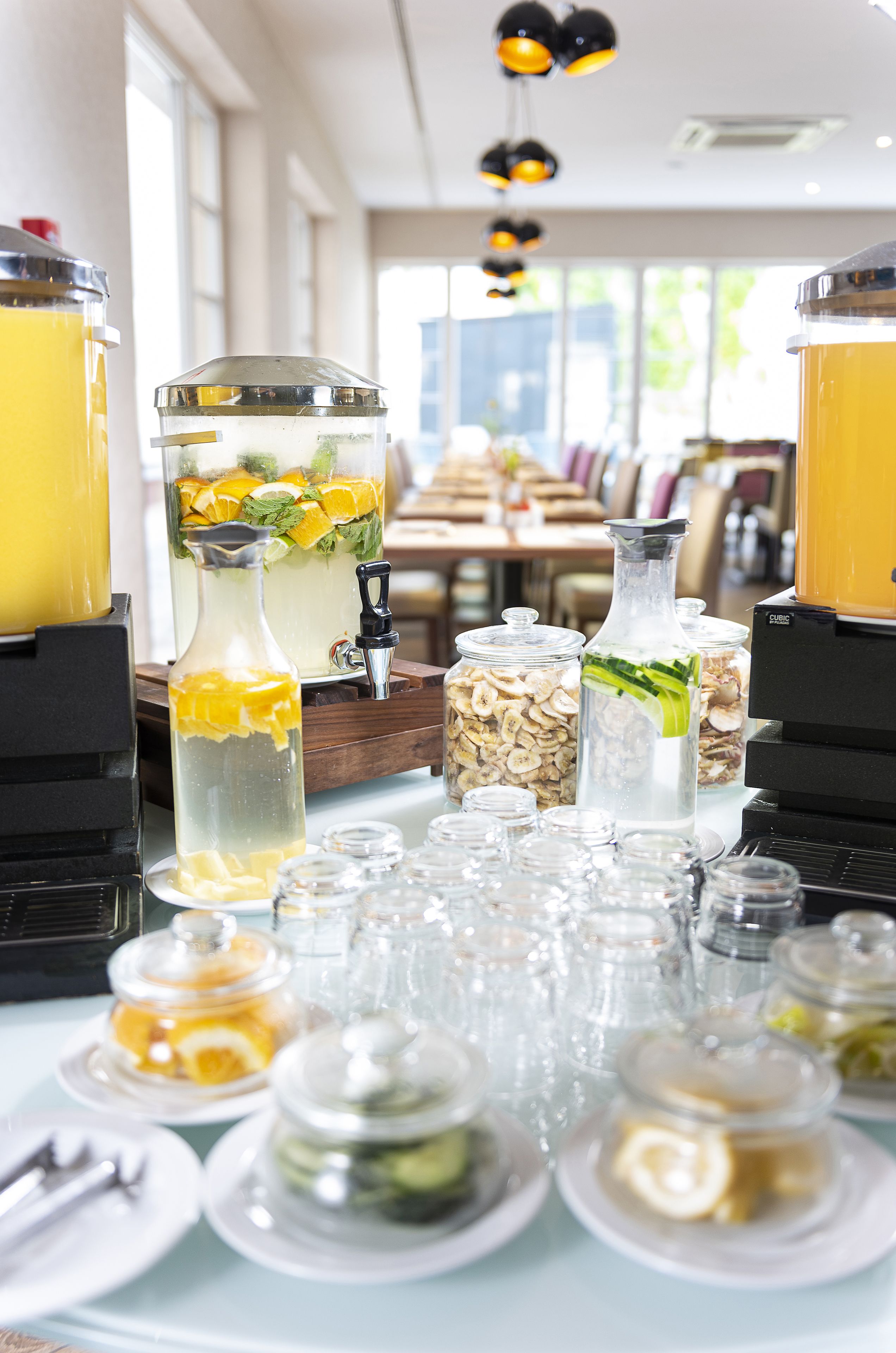 Una mesa con varios recipientes de comida y bebida, incluyendo una jarra con rodajas de naranja y menta, una botella con rodajas de pepino y varios frascos con diferentes ingredientes.