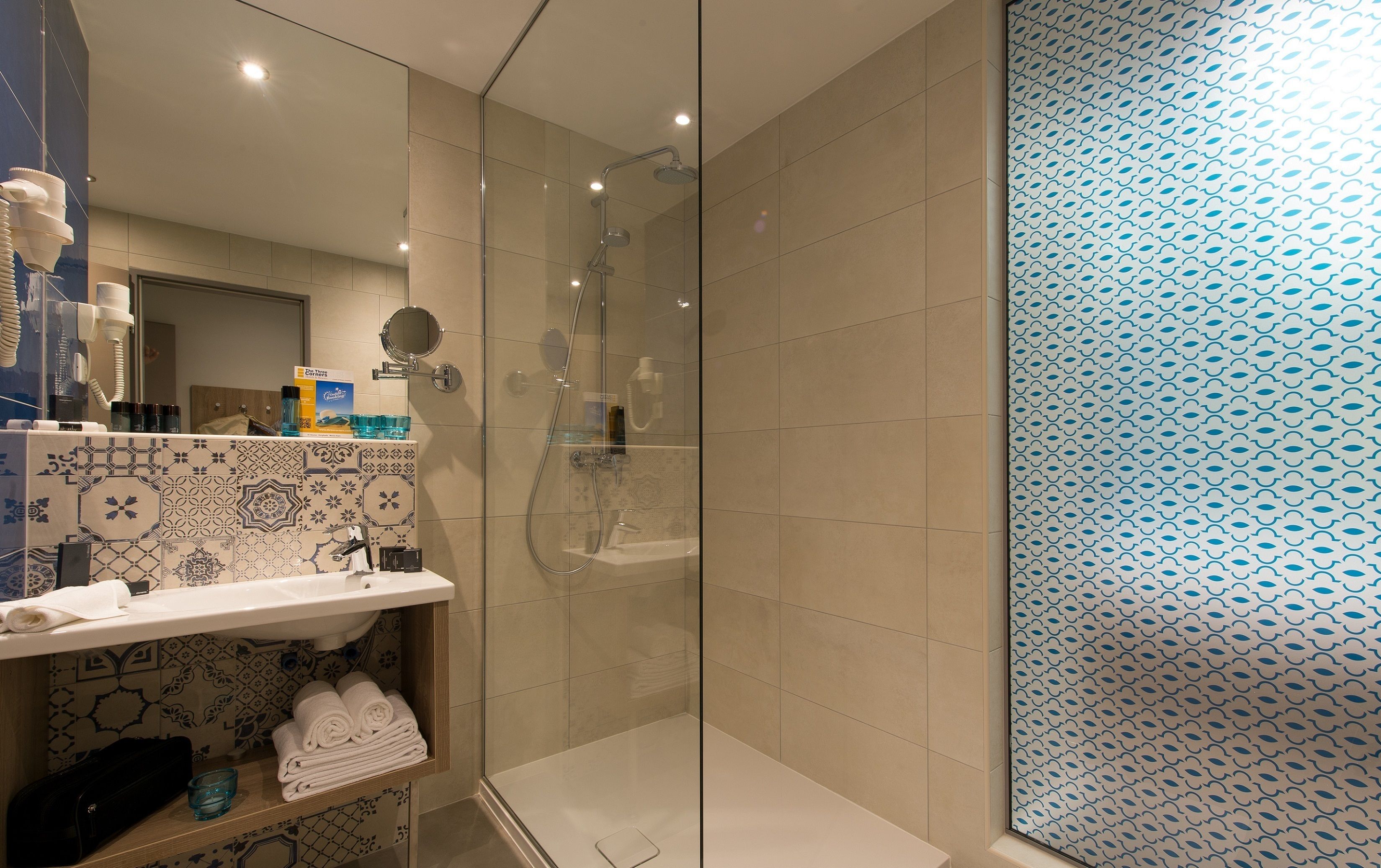 A modern bathroom with a glass-enclosed shower, a sink with a decorative tile backsplash, and a shelf with towels and toiletries.