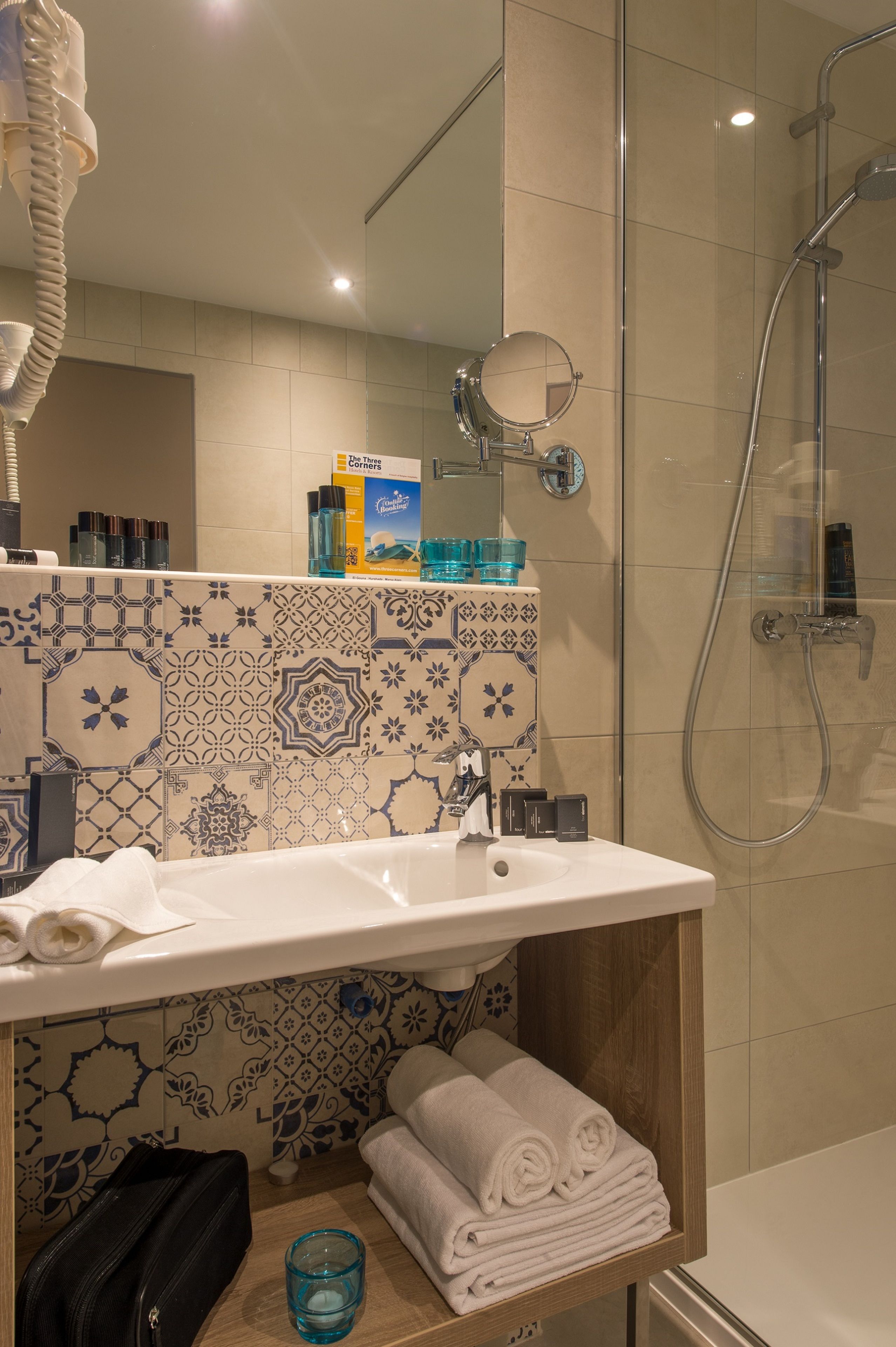 Un baño con lavamanos, espejo y ducha. Hay toallas y artículos de aseo en la encimera.