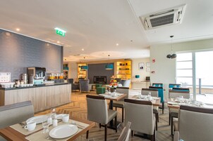 A modern hotel lobby with a dining area, a kitchen, and a TV.