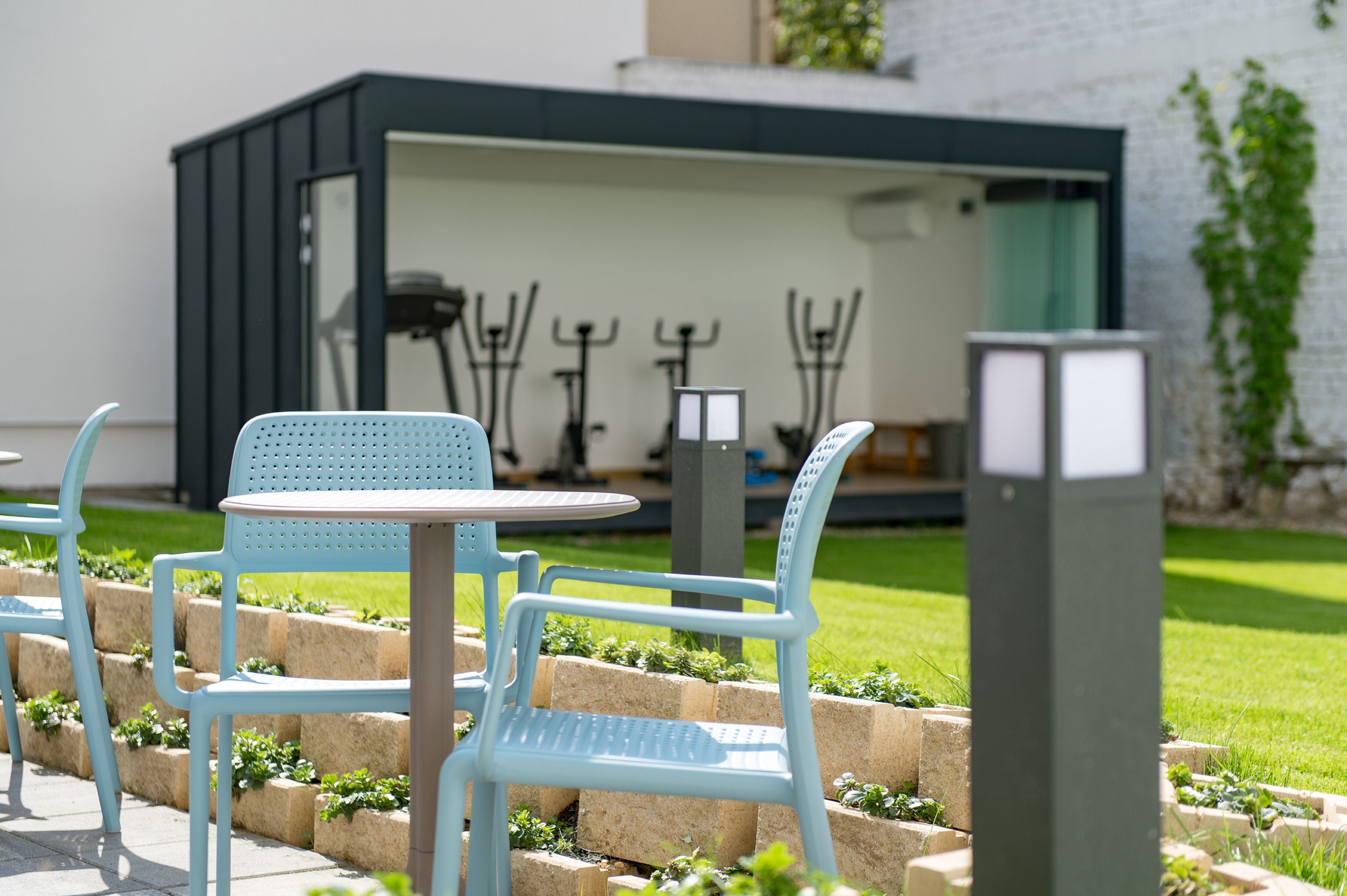 A patio area with light blue chairs and a table, a small outdoor kitchen, and a brick planter with greenery.