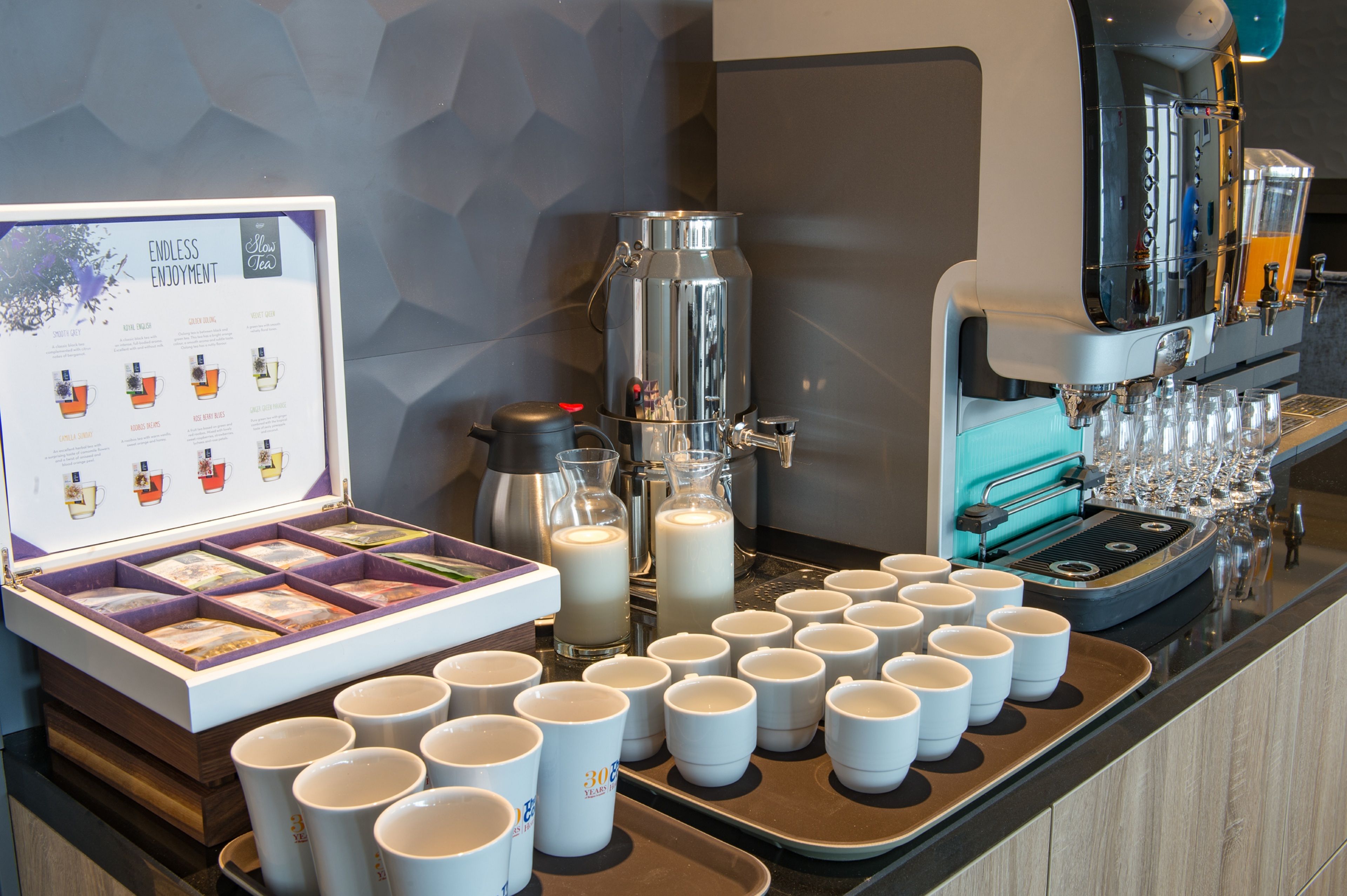 A coffee station with a coffee machine, milk dispensers, and a tea display.
