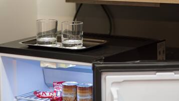 Un área de cocina con cafetera, un plato de fruta y un refrigerador lleno de bebidas.