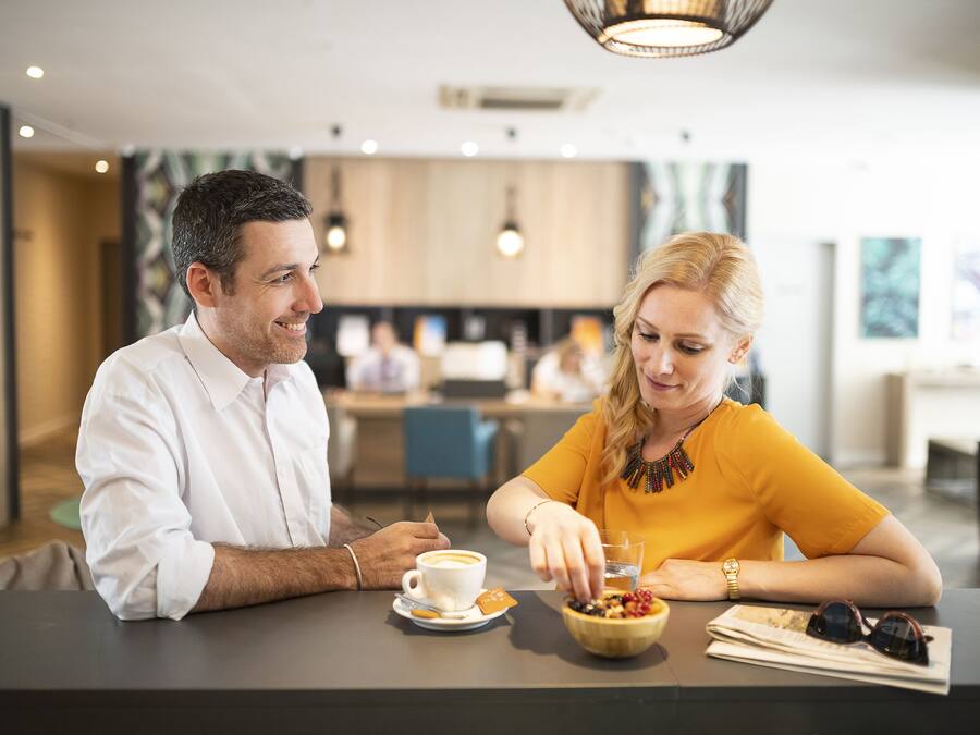 Un comedor moderno con una pareja sentada en una mesa, una taza de café y un bol de fruta.