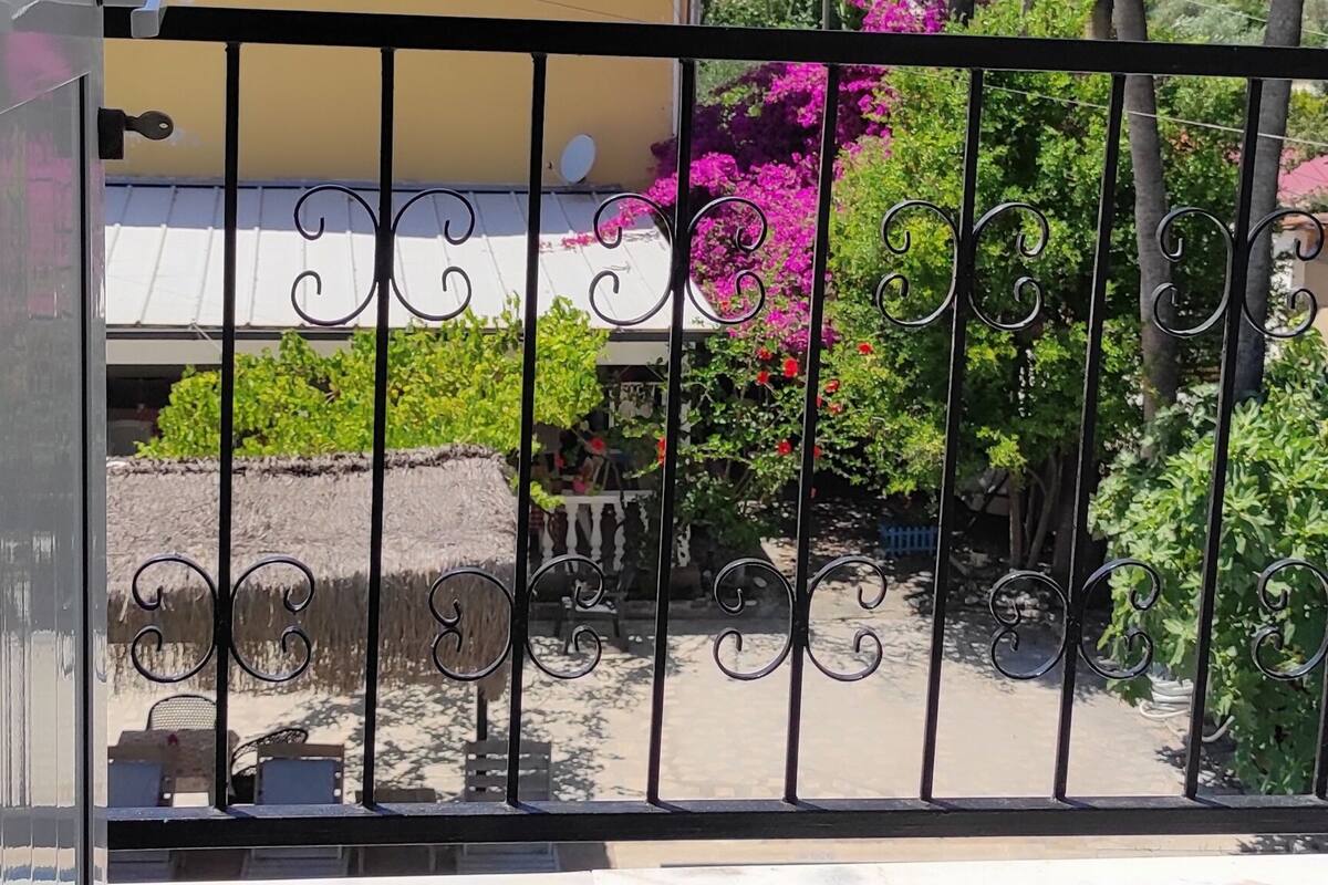 Ein Balkon mit Metallgeländer, ein gelbes Gebäude im Hintergrund und ein Gebirge.