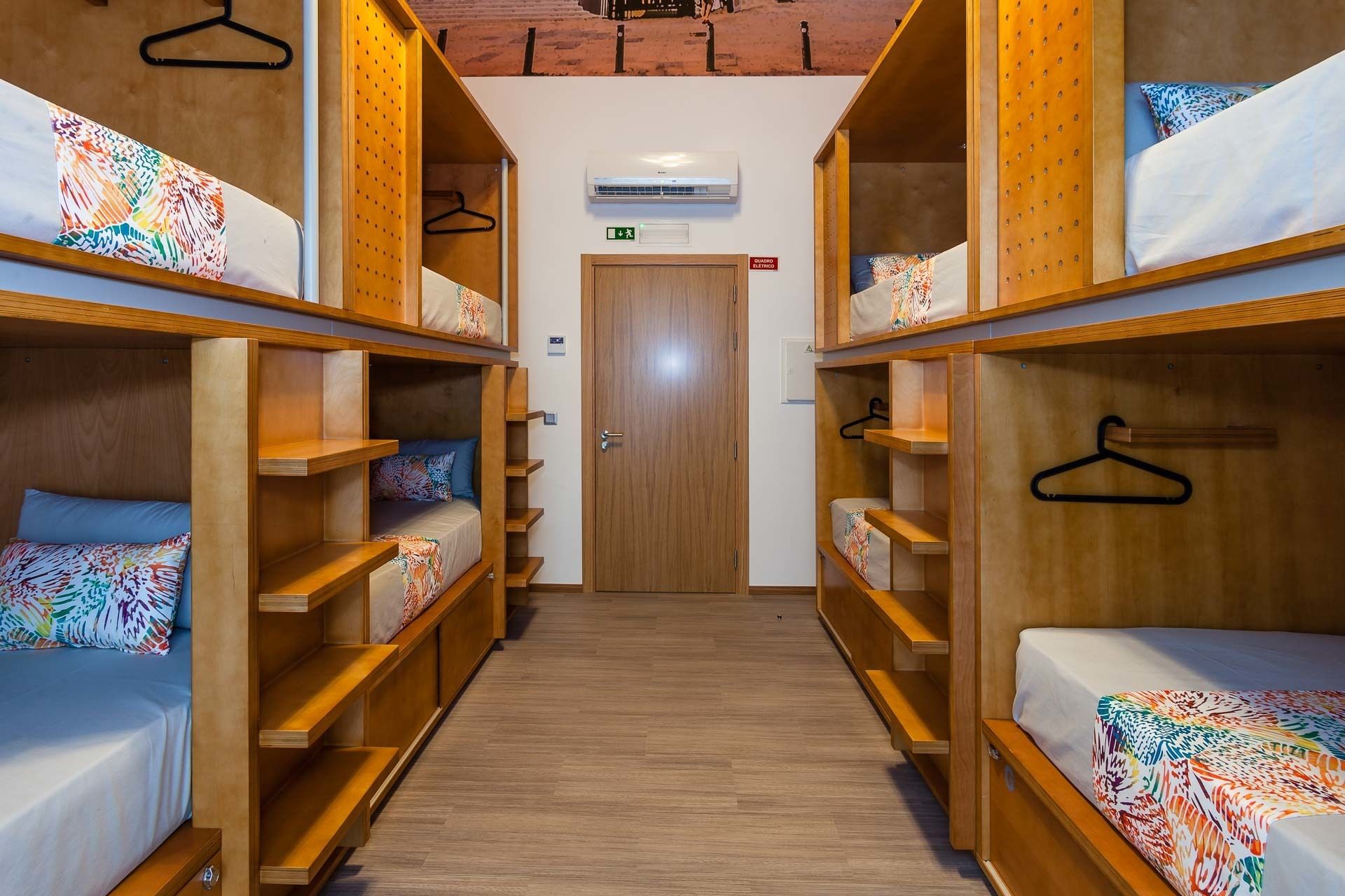 A dormitory room with bunk beds, wooden shelves, and a door with an emergency exit sign.