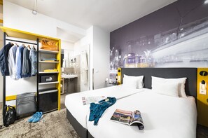 Habitación de hotel con cama, armario, escritorio y un mural con vista a la ciudad.