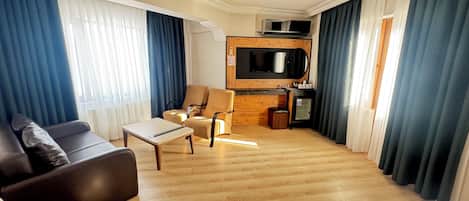 A hotel room with a sofa, a small table, a chair, a microwave, and a TV mounted on the wall.