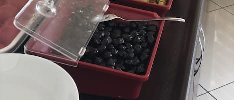 Un bufé con diversas opciones de comida, incluyendo frutas, verduras y aceitunas.