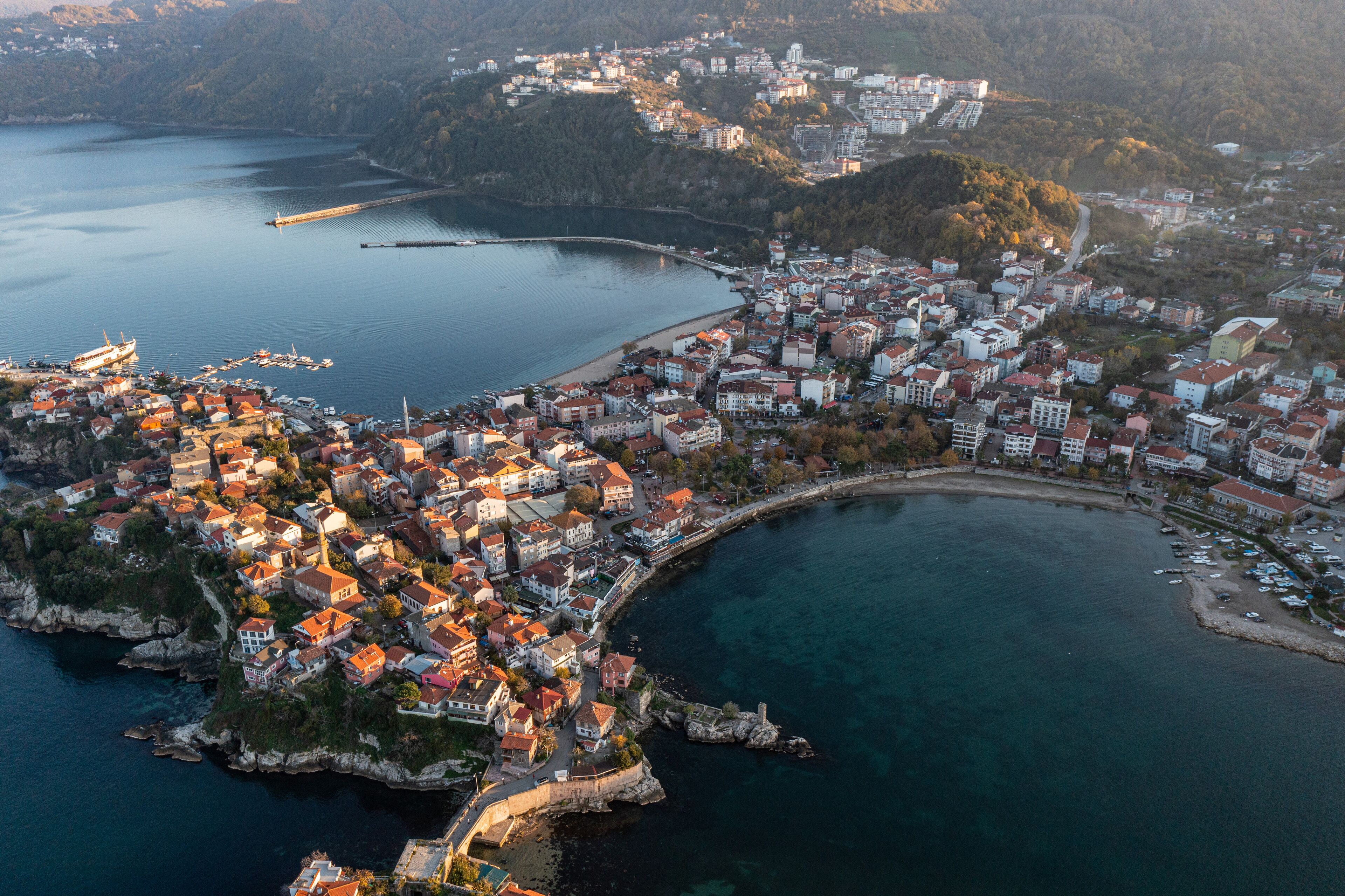 An aerial view of a coastal town with a mix of residential and commercial buildings, a marina, and a bridge connecting the town to the mainland.