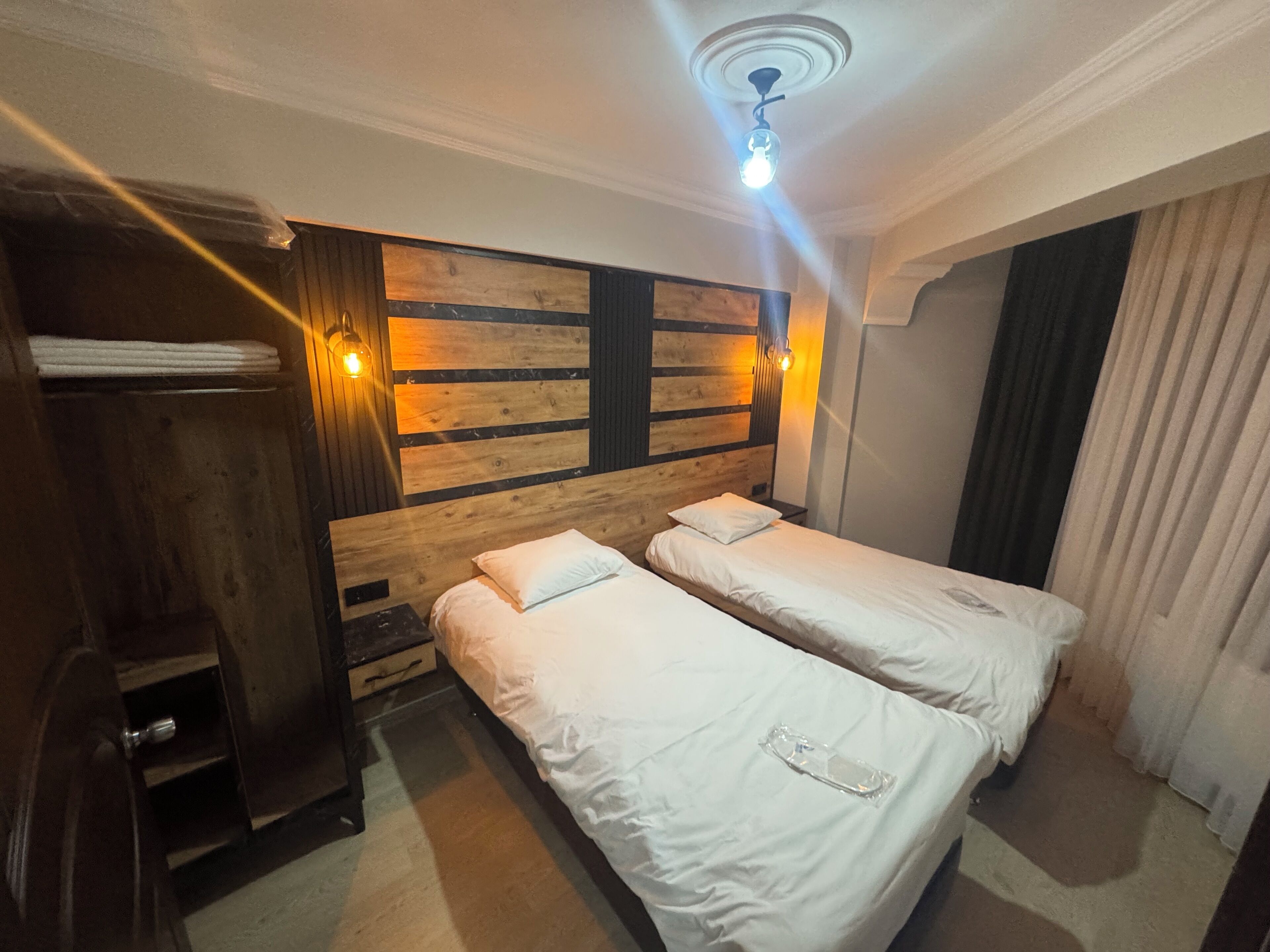 A room with two beds, wooden headboard, wall-mounted lights, and a ceiling fan.