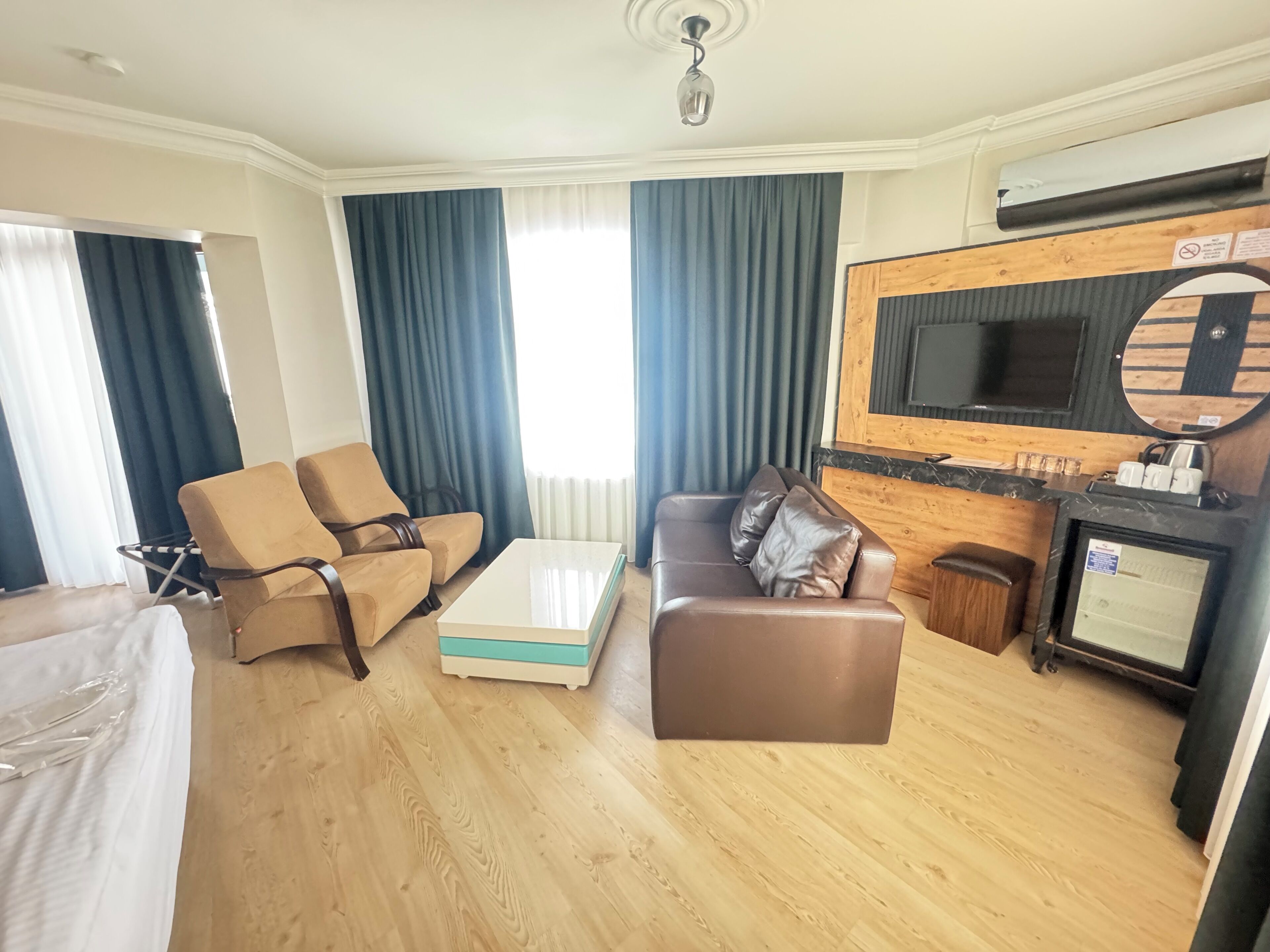 A hotel room with a sofa, a coffee table, a TV mounted on a wooden wall, and a small kitchenette.