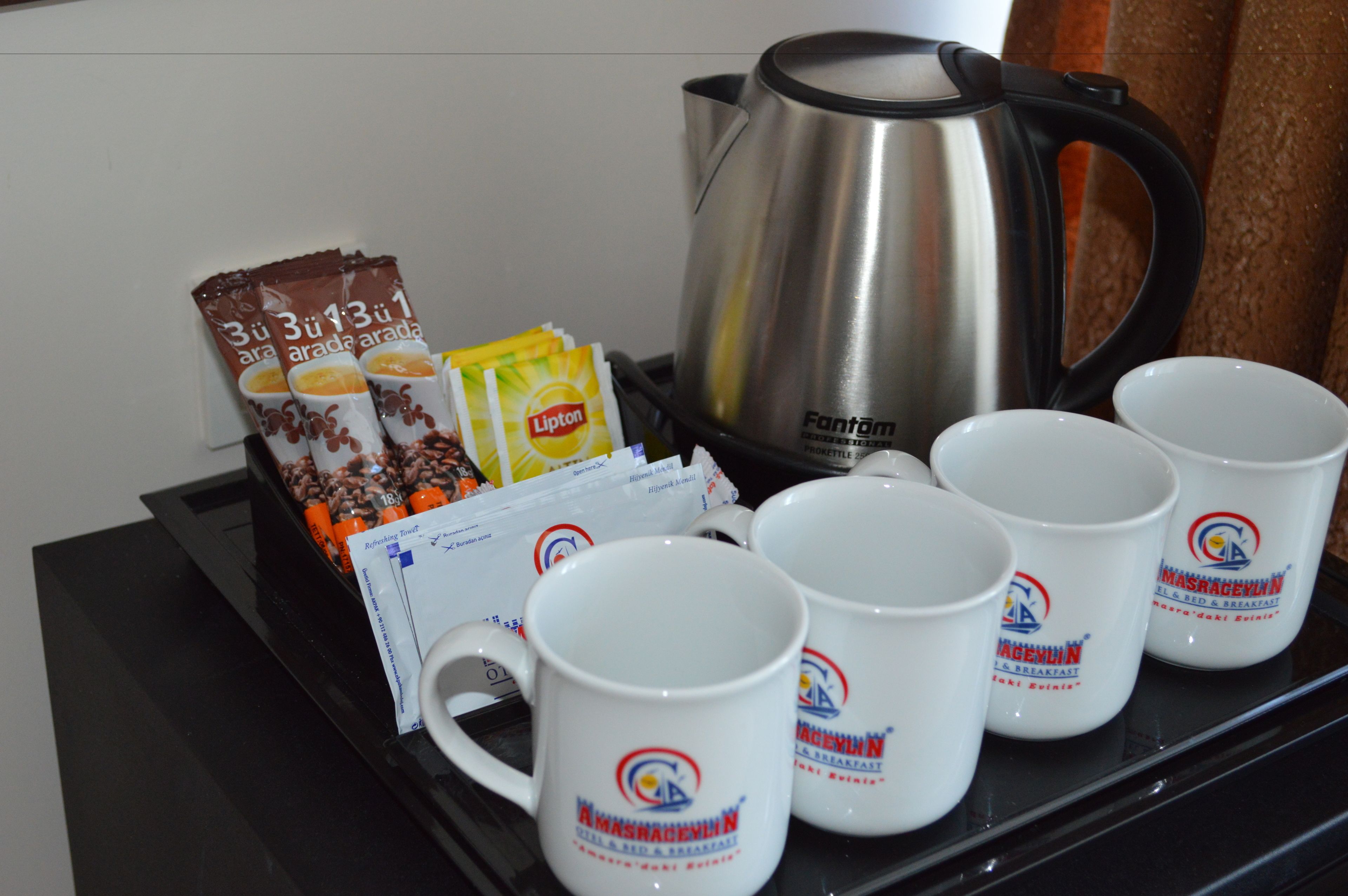A tray with coffee packets, Lipton tea bags, a kettle, and branded mugs.