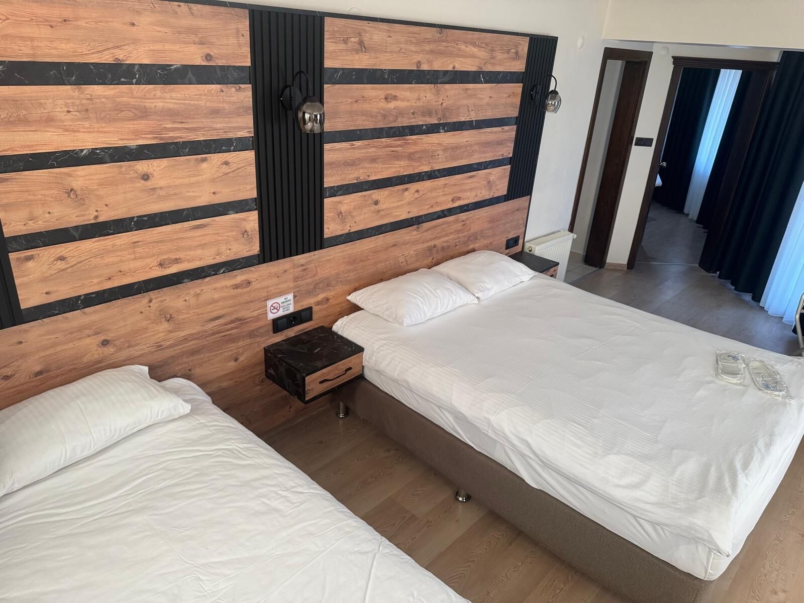 Ett hotellrum med två sängar, en sänggavel i trä, ett nattduksbord och en vägglampa.