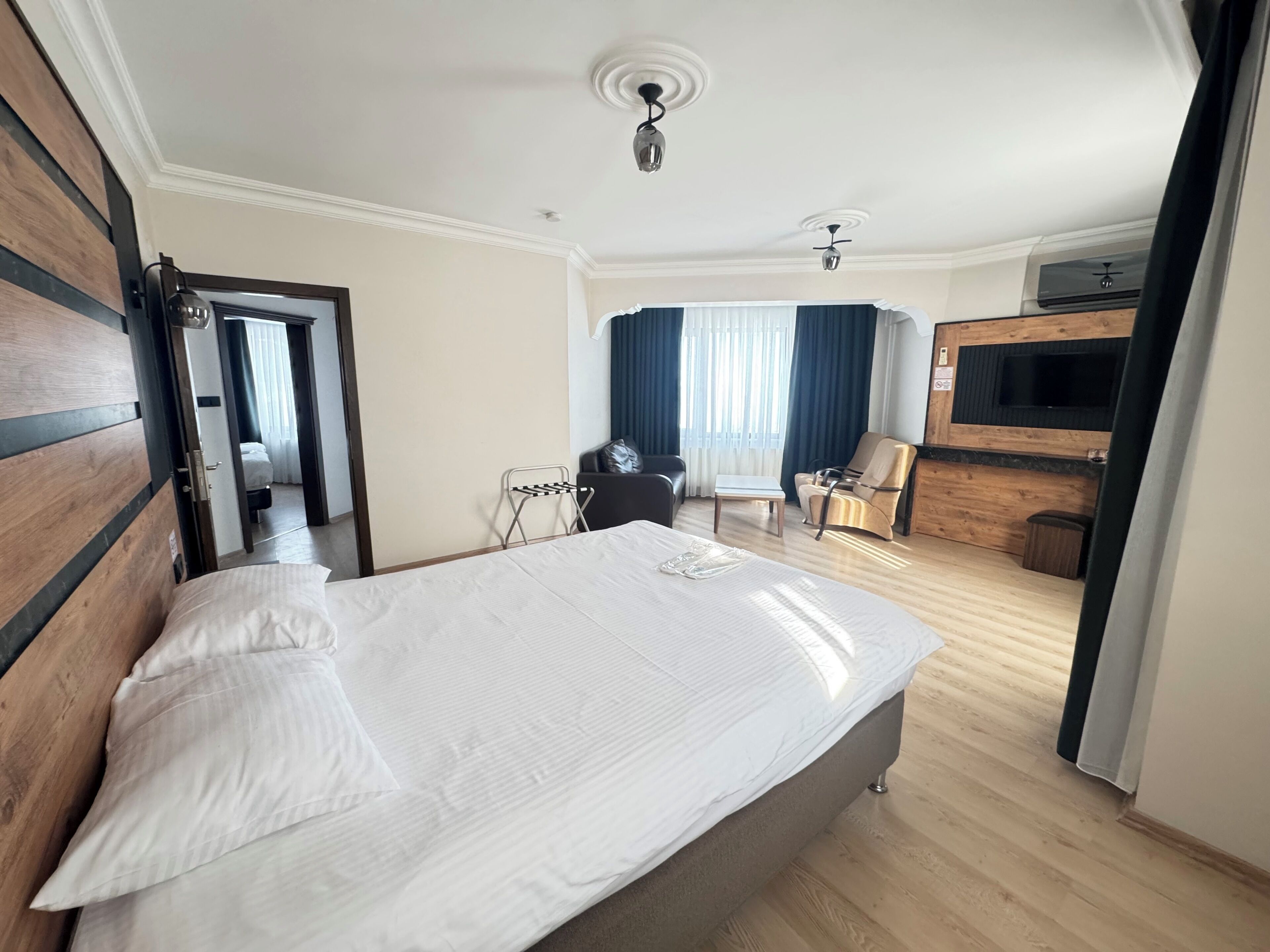 A hotel room with a large bed, a desk, a chair, a TV, and a wardrobe.