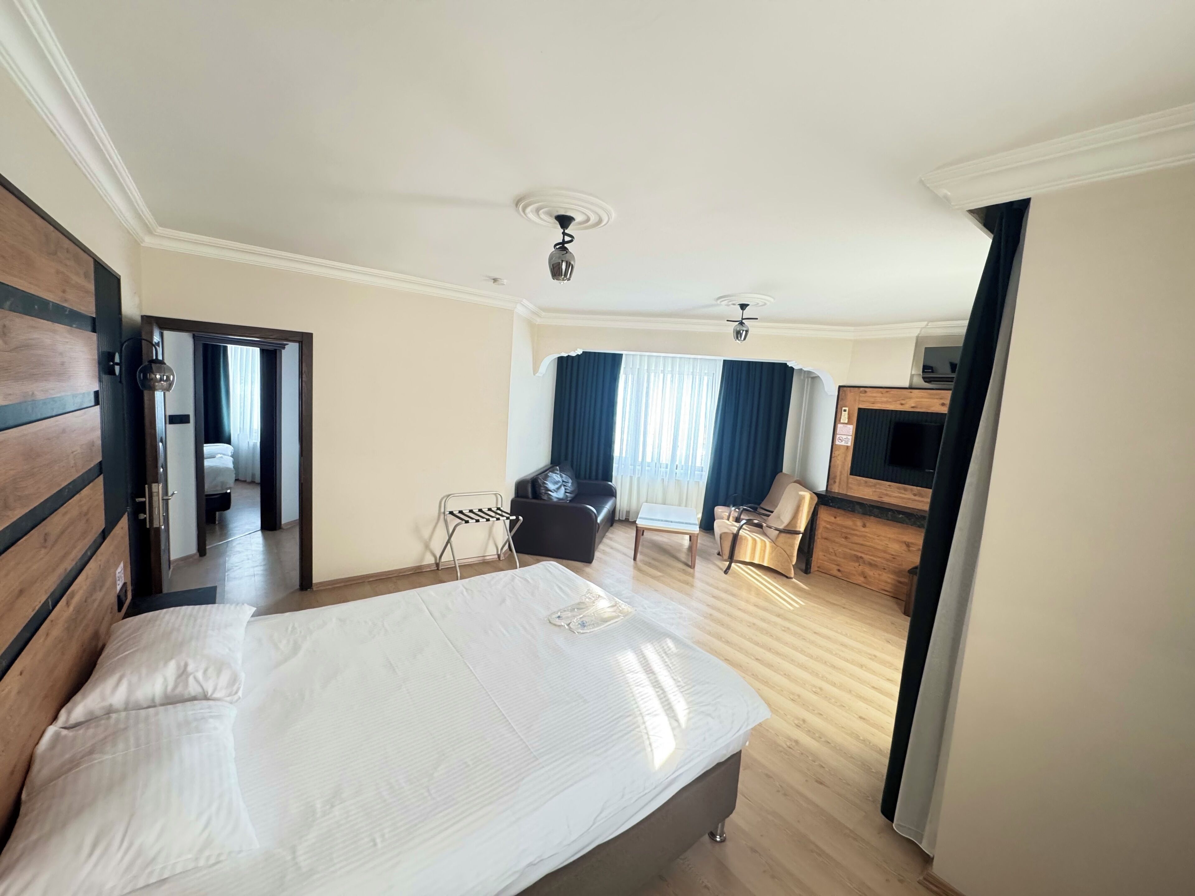 A hotel room with a large bed, a desk, a chair, a TV, and a view of the hallway.