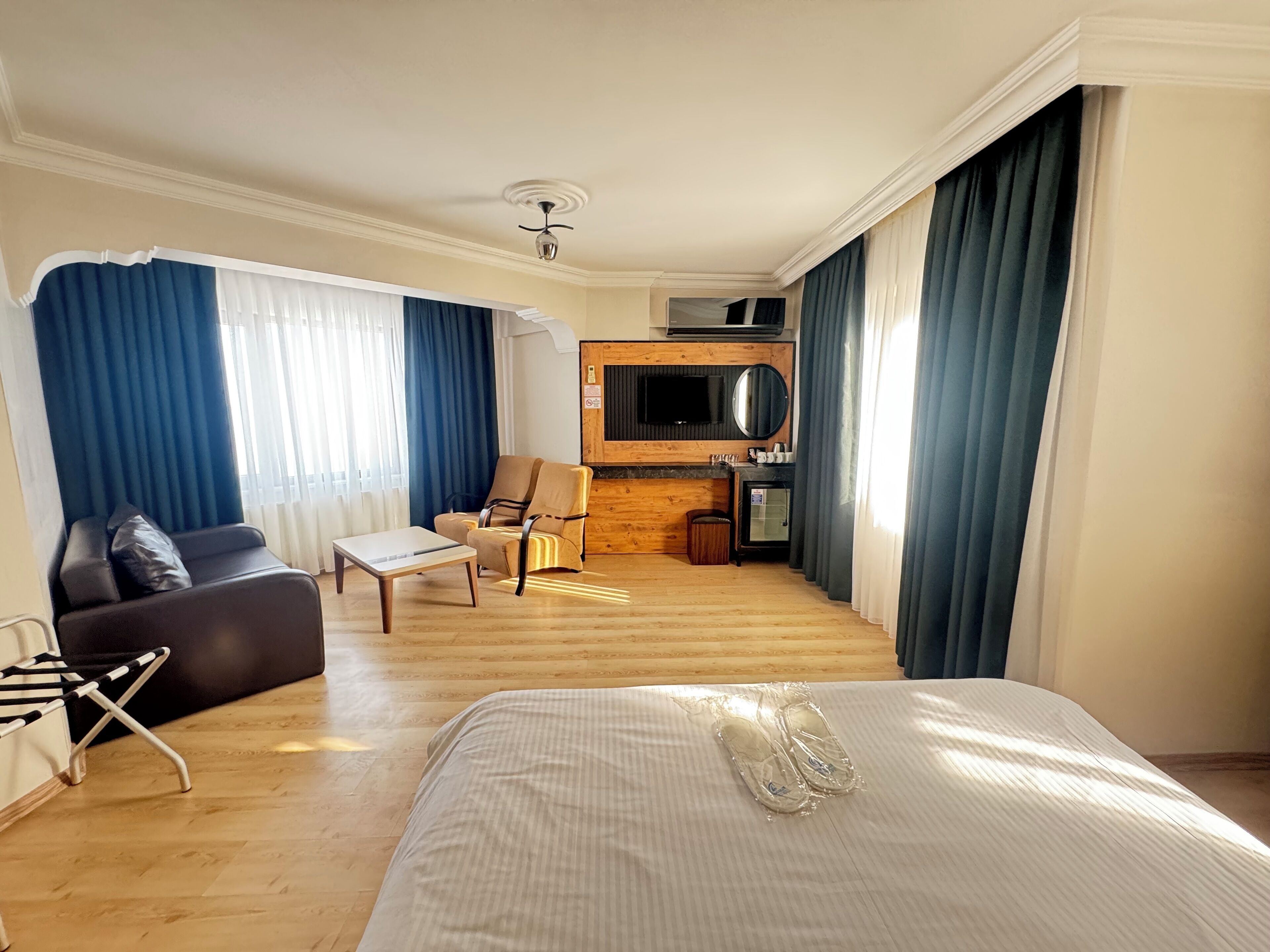 Quarto de hotel com cama, sofá, mesa de jantar, cadeira, pequena área de cozinha e televisão.