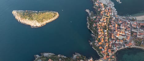 An aerial view of a coastal town with a prominent peninsula, a marina, and a densely packed residential area with red-roofed buildings.