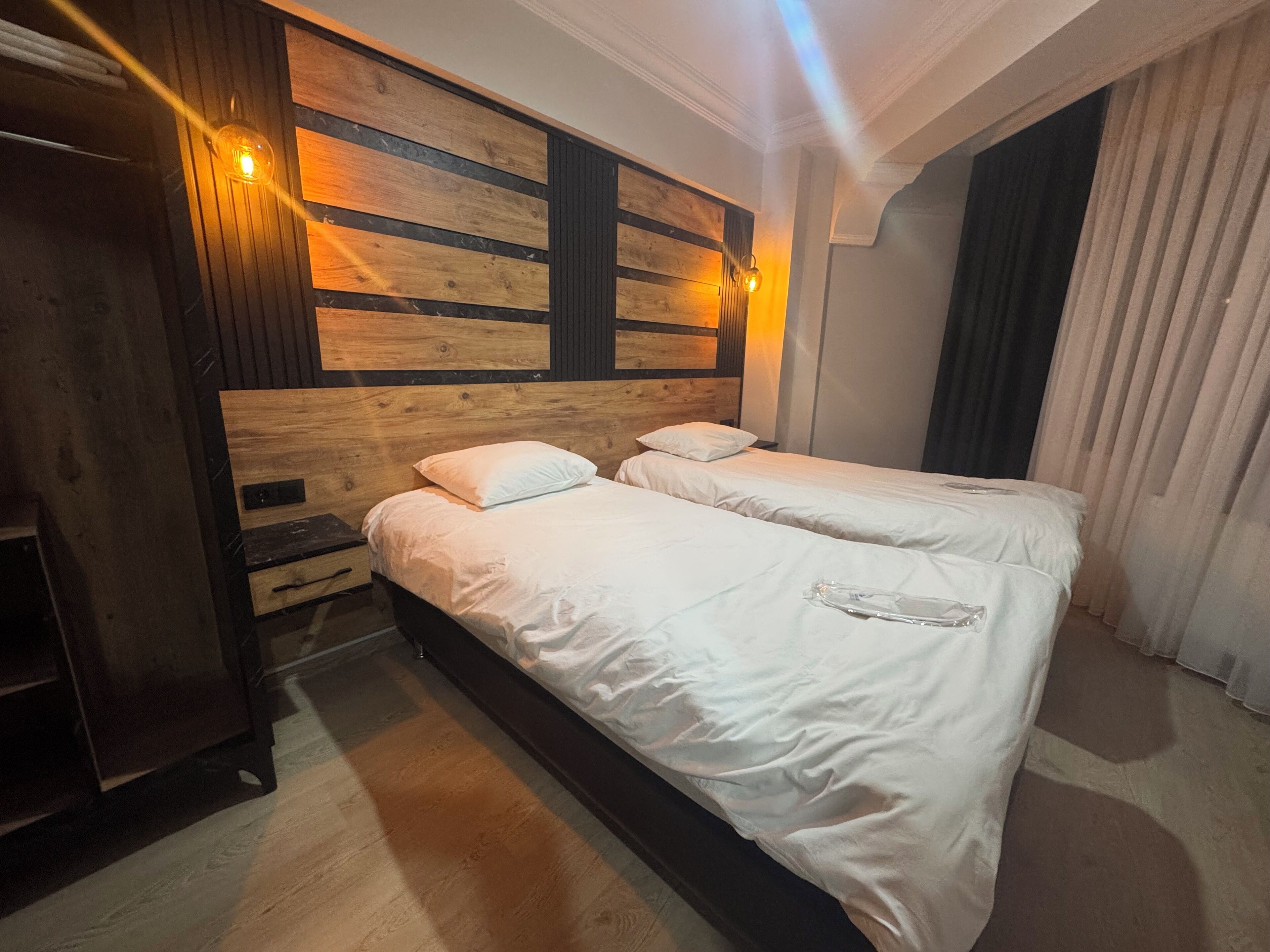 A room with two beds, wooden headboard, bedside tables, and a large window with curtains.