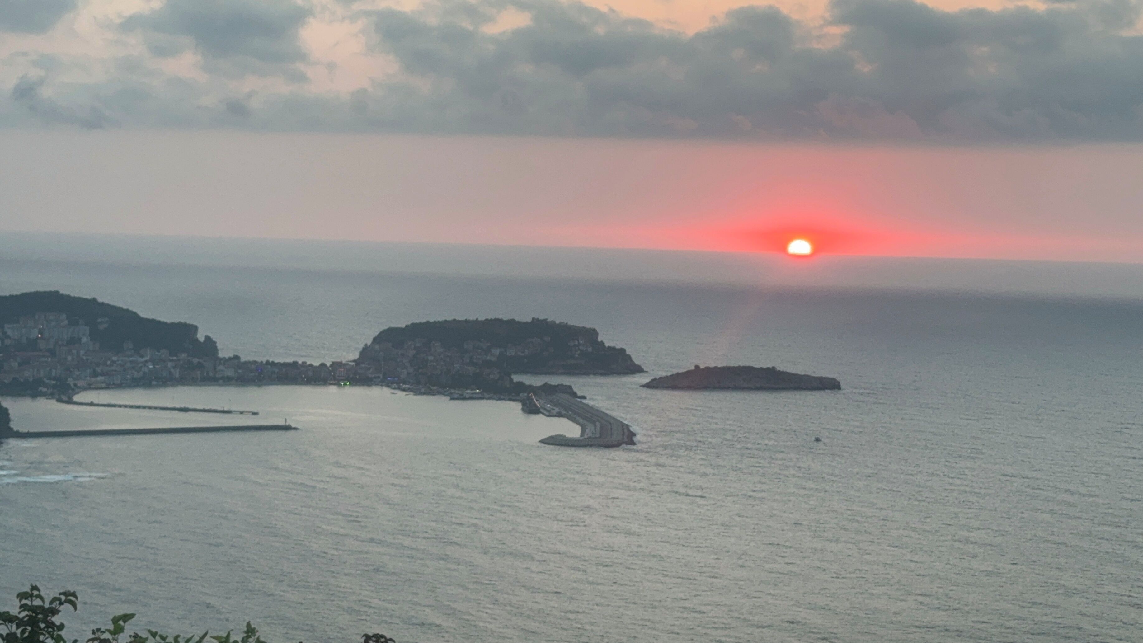 Un paisaje costero con un atardecer sobre el mar, que presenta afloramientos rocosos y un pueblo lejano.