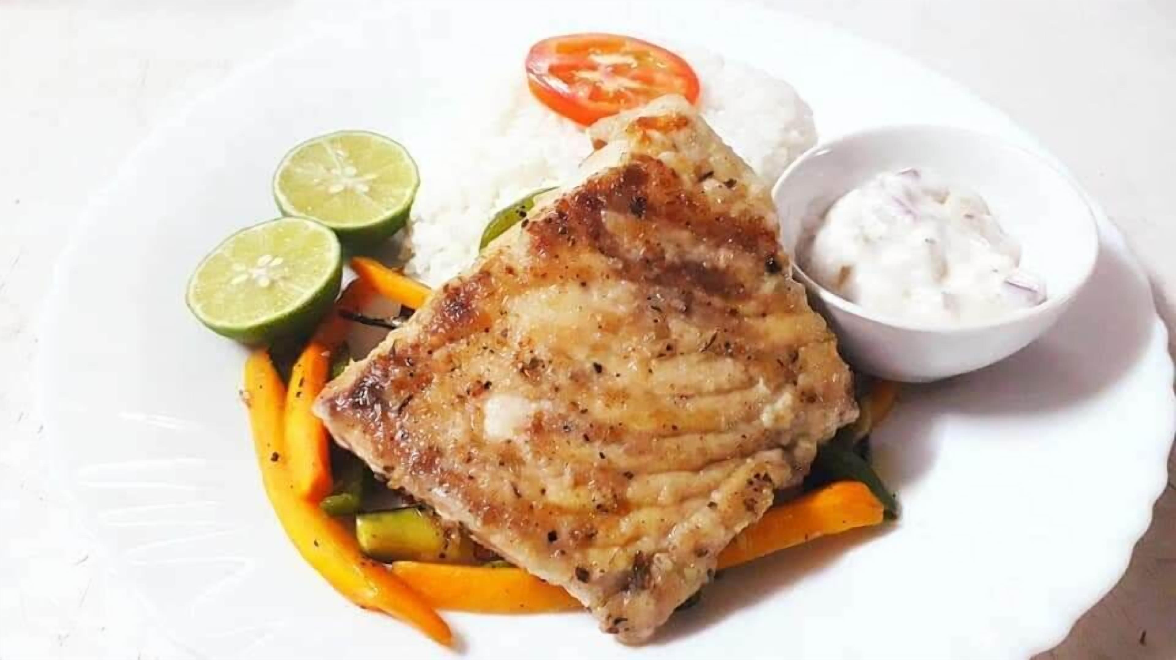 A plate with grilled fish, rice, vegetables, and a side of sauce.