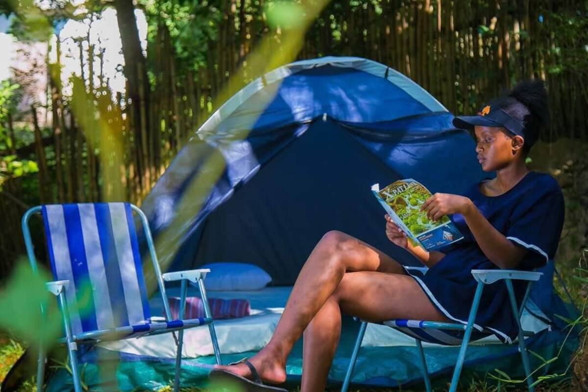 Une tente, une personne lisant un livre, une chaise à rayures et un décor naturel.